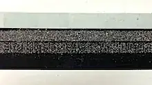Image of magnetic stripe with iron filings sticking to two tracks, with enough resolution to show spaces and marks on tracks