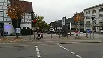 Nur Hinweisschild. Die Zufahrt ist durch einen oder mehrere Poller gesichert. Die Aufstell- und Bewegungsfläche befindet sich, nicht markiert, auf dem Platz dahinter.