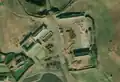 5/6 Farmyard (landuse=farmyard) composed of long buildings, surrounded by a fence dotted with hay piles, close to a road (Maxar satellite imagery).