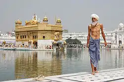 A Sikh pilgrim stands in the foreground, while in the background the Golden Temple (Harmandir Sahib) is plainly visible.